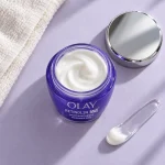 نمای بالای کرم شب اولای Retinol 24 MAX در ظرف باز کنار درِ نقره‌ای و کاردک